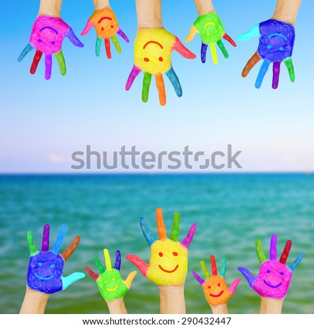 Frame of children hands painted with smiling faces against sea and sky background. Summer vacation concept.