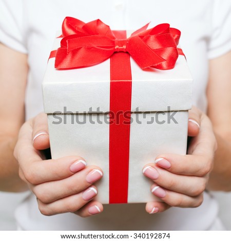 Female hand holding a gift box with a red bow. Time gifts. Selective focus on the present.