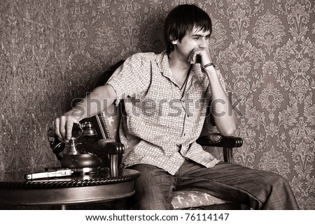 Laughing man sitting beside an antique table, on which the old phone and gun