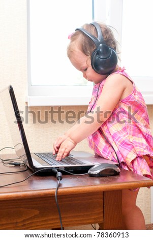 Cute baby girl listening to a music and working on the laptop