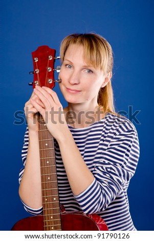Beautiful middle aged blonde woman in a striped vest posing with a red guitar. Isolated on blue background with clipping path.