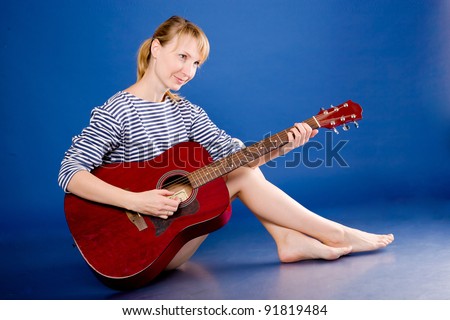 Beautiful young blonde woman in a striped vest posing with a red guitar. Isolated on blue.
