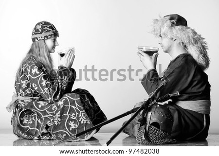 Black and white portrait. A couple of Mongolian national costume drinking tea from cups. At the feet of men - a helmet and swords. Retro.