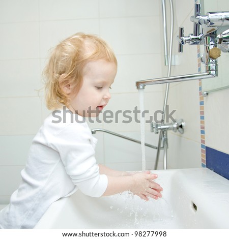 blond baby girl washing hands and face in the morning in the bathroom. The girl wearing a blank white shirt. Ready for your design or logo
