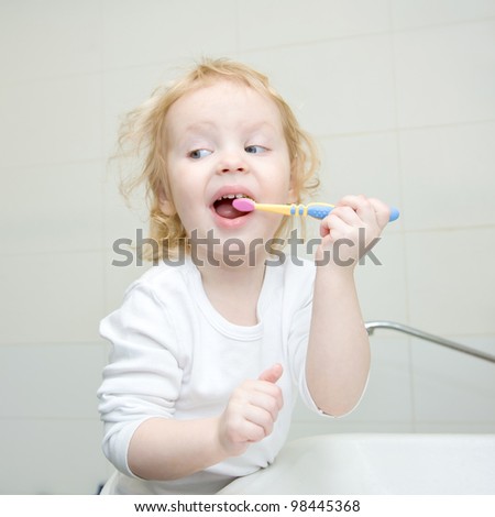 The little blonde girl brushing her teeth with a toothbrush in the bathroom. Hygiene. The girl wearing a blank white shirt. Ready for your design or logo