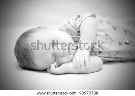 Newborn baby boy sleeping with his hands under his cheek on white blanket. Black and white. The symbol of Innocence