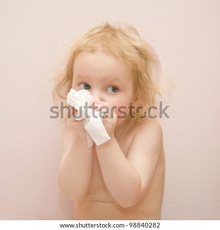 Lovely blond curly-haired baby girl with blue eyes is sick. She has a runny nose. Blowing his nose with disposable tissues. Isolated on pink background