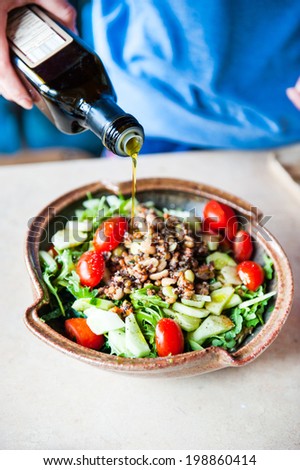 pouring olive oil on salad with tomato and cucumber