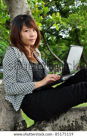 Portrait of beautiful woman sitting on the tree and playing laptop