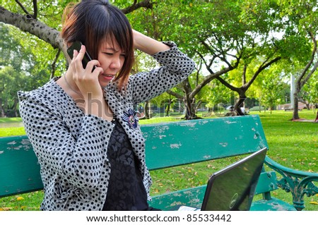 A stressed woman talk mobile phone with laptop in nature