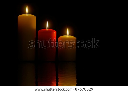 Three candles over a black background and its reflection