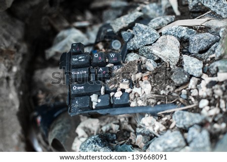 broken black keyboard lying on the garbage under the stone