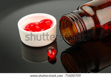 Red vitamin pills in vial on glossy black background