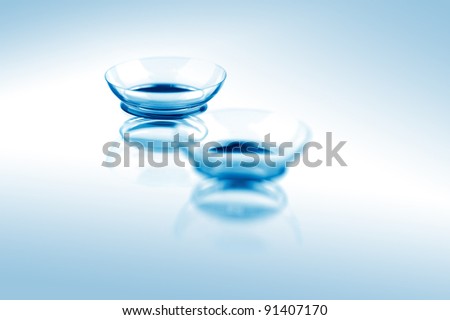Two contact lenses with reflections on blue surfaces. Focus on long-distance lens.