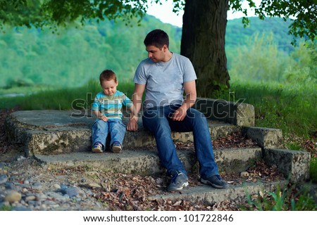 father and son sitting on stairs under an old tree. family ties concept