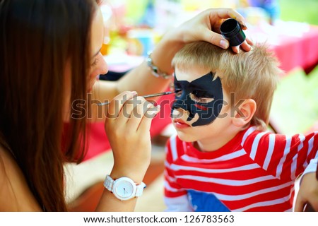 Woman Painting Face Of Kid Outdoors