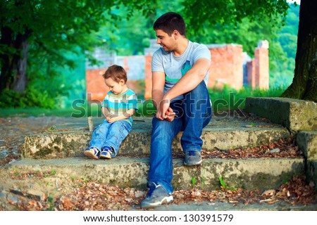 father and son talk, while sitting on old stairs among trees