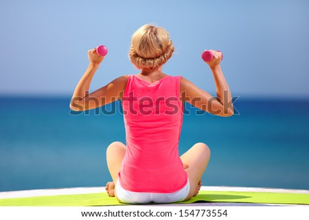 young woman doing exercises with hand weights on the beach
