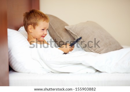 happy kid watching tv cartoons in bed