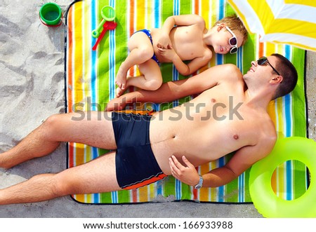 happy father and son sunbathing on colorful blanket