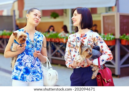 happy women talking on crowded city street, hold Yorkshire Terrier