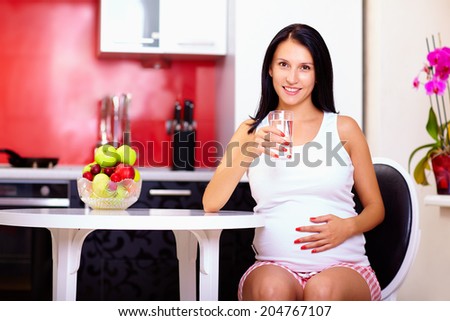 pregnant woman drinking water in kitchen