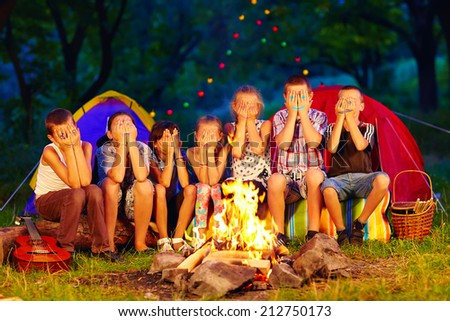 funny kids with painted faces on hands sitting around camp fire