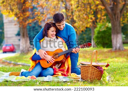man teaching girl play a guitar on autumn picnic