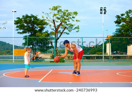 father and son playing basketball on sport ground