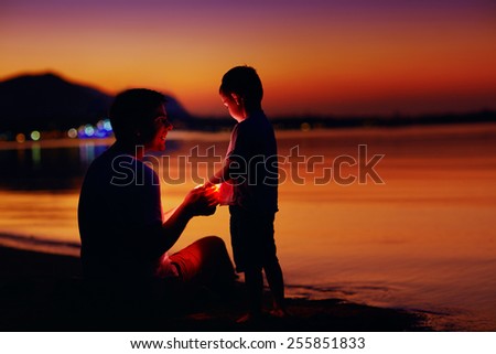 happy father and son with lantern at sunset beach