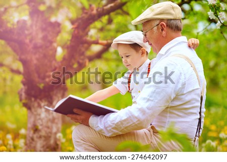grandfather with grandson reading book in spring garden