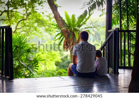 father and son sitting on tree house stairs in tropical forest