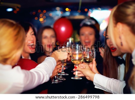 happy elegant women clinking glasses in limousine, focus on glasses