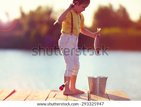 out of focus young little boy caught a fish on the hook, on pond at sunset