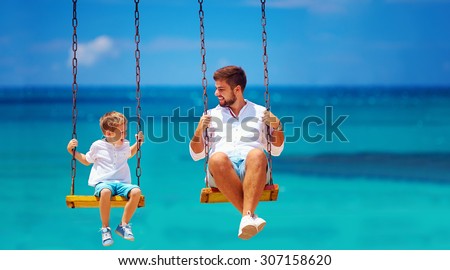 joyful father and son having fun on swings, sea background