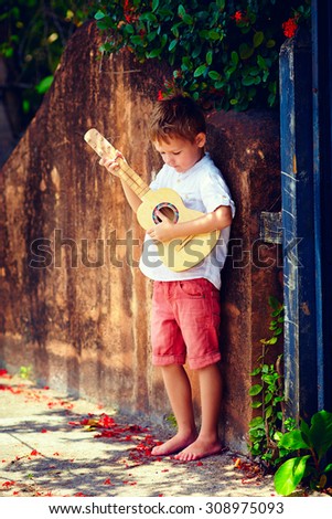 cute young boy playing guitar near the summer old fence