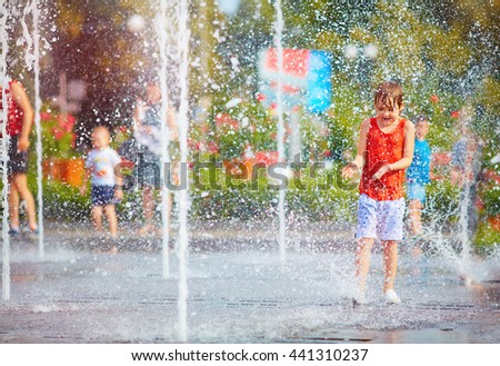 excited boy having fun between water splashes, in fountain. Summer in the city