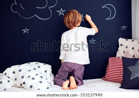 cute kid in pajamas painting chalkboard wall in his bedroom.