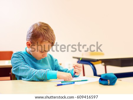 cute boy with special needs writing letters while sitting at the desk in class room