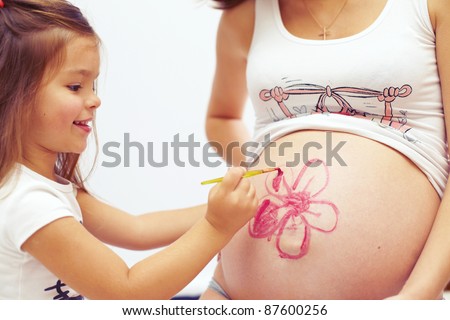 close-up portrait of cute daughter painting  mom\'s beautiful belly