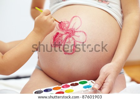 close-up portrait of cute daughter\'s hand  painting  mom?s beautiful belly