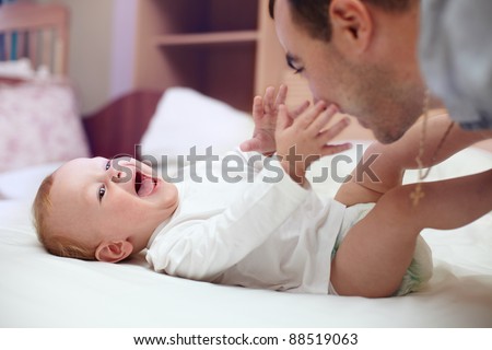 Young happy father playing  with baby. Man and baby are lying in bed. baby want to catch father\'s face