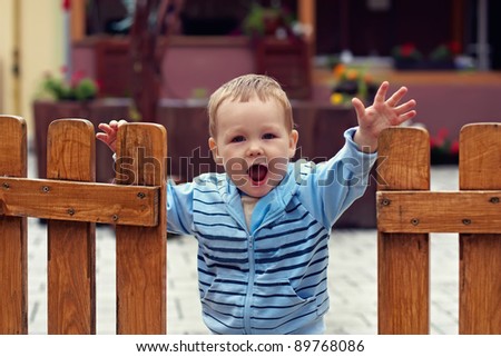 Cute boy stands in an open wooden fence with a welcome expression on his face
