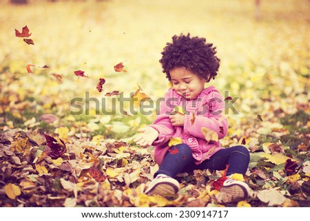 Adorable african american mixed race kid wearing casual clothes playing in park with bunch of leaves, enjoying warm autumn day