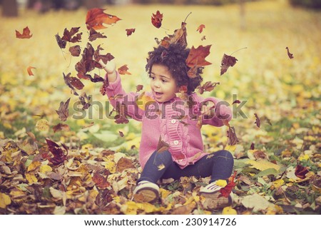 Adorable african american mixed race kid wearing casual clothes playing in park with bunch of leaves, enjoying warm autumn day
