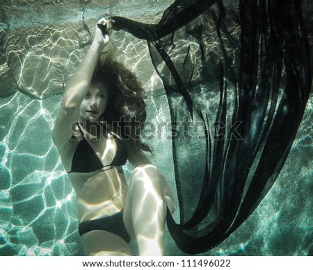 Pretty young woman floating underwater in a black Bikini