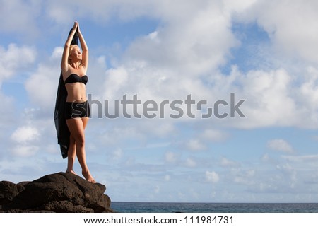 Beautiful Woman on Lava Rocks at the Ocean arms up above her head