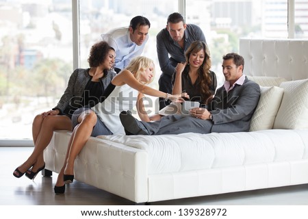 Group of young diverse ethnicity people getting together after work before a party sharing ideas on a mini touch pad