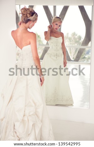 Elegant Reflection of a Beautiful blond bride in mirror in modern glass building penthouse