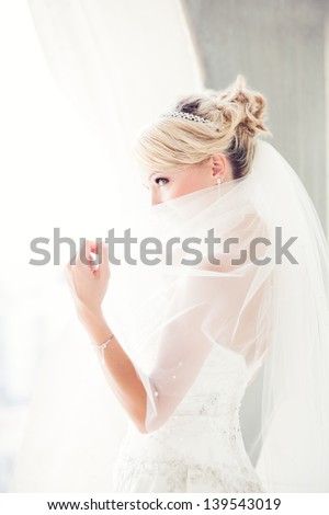 Gorgeous Smiling Blonde Bride In Front Of A Penthouse Window At A Modern Hotel Peaking Over Her Veil